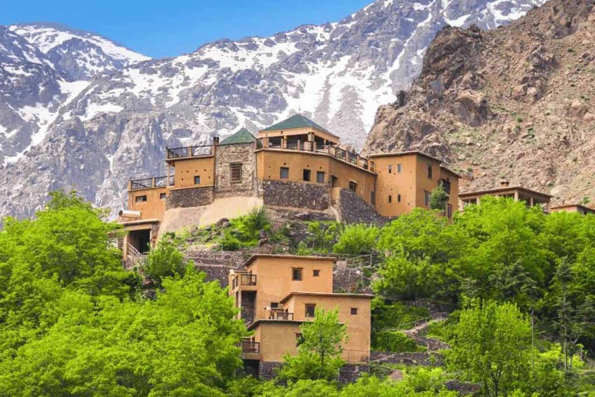 Hikers trekking on a trail in the High Atlas Mountains with snow-capped peaks in the background.