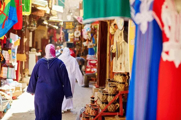 Two Moroccan women in traditional djellaba walking through a medina.