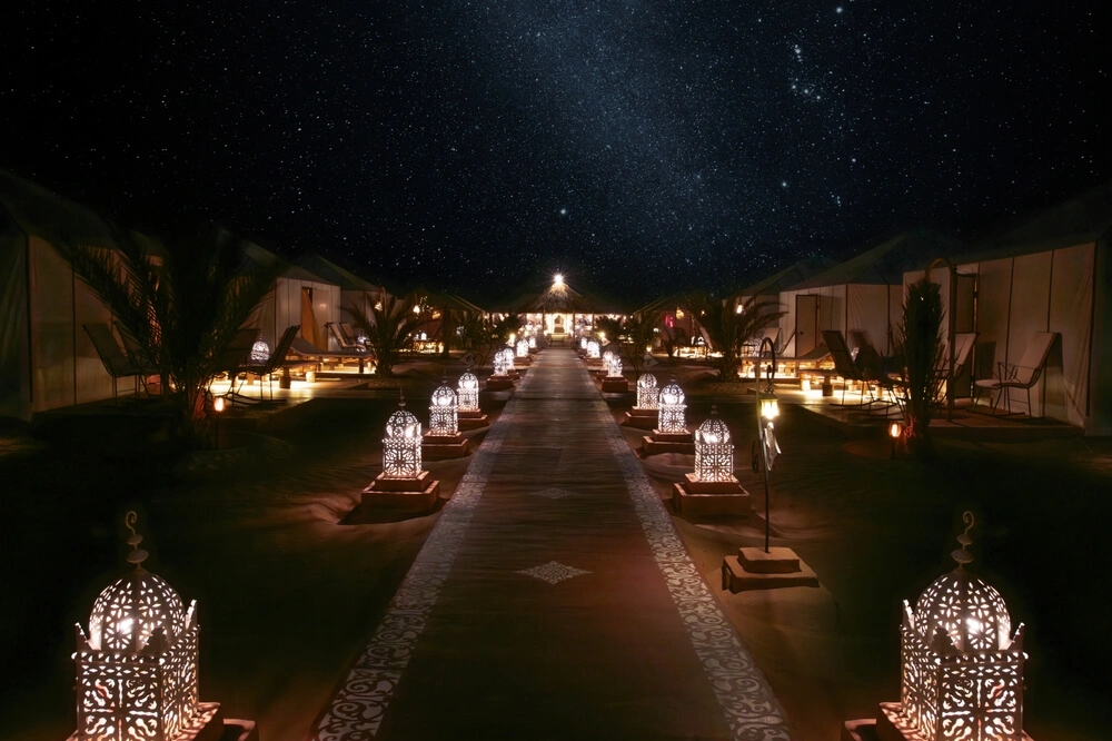 Un lujoso campamento en el desierto de Marruecos iluminado por la noche bajo las estrellas.